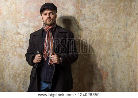 image of a caucasian man with grungy blond hair dressed warmly in a stylish black trench coat and a funky hat and scarf for the cold winter