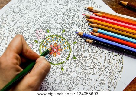 Anti-stress coloring book in the drawing process. Woman paints the razukrashki on the table are colored pencils and tea coffee