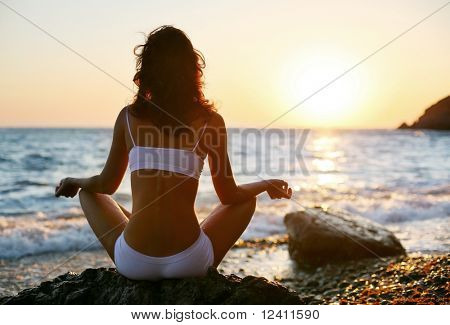 Vrouw die mediteren op het strand bij zonsondergang.