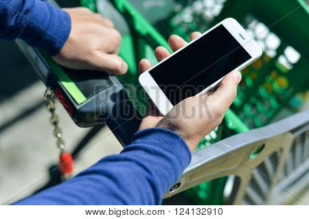 Cellphone and cart on store goods background. Closeup on person holding mobile smart phone in hand during shopping.