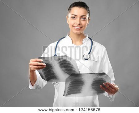 Young female doctor holding radiograms on grey background