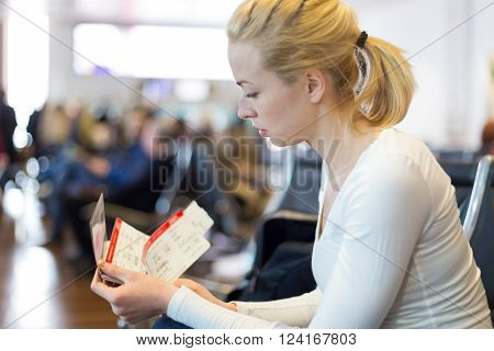 Young blond caucsian woman waiting on airport departure gates to board a plane with tickets in her hands.