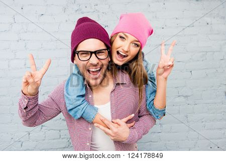 Happy Cheerful Man And Woman Embracing, Gesturing With Two Fingers And Screaming