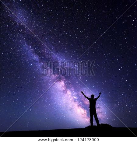 Landscape with colorful purple Milky Way. Night sky with stars and silhouette of a happy man with raised up arms on the mountain. Beautiful Universe. Space background