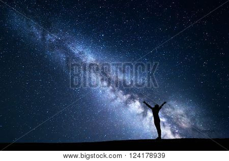 Landscape with blue Milky Way. Night sky with stars and silhouette of a standing sporty girl with raised-up arms. Beautiful Universe. Space background