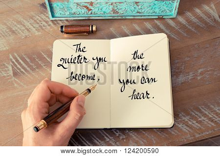 Retro effect and toned image of a woman hand writing on a notebook. Handwritten quote The quieter you become, the more you can hear as inspirational concept image