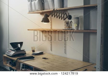 Rustic desktop in professional artisan roastery with empty wooden table with handle sealing machine on it ready to work. White packages on shelves above table and old vintage lamp with warm light film effect
** Note: Soft Focus at 100%, best at smaller s