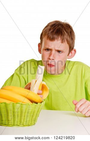 Unimpressed young boy eating a fresh banana with a look of horror on his face as he chews the first mouthful while seated at the table