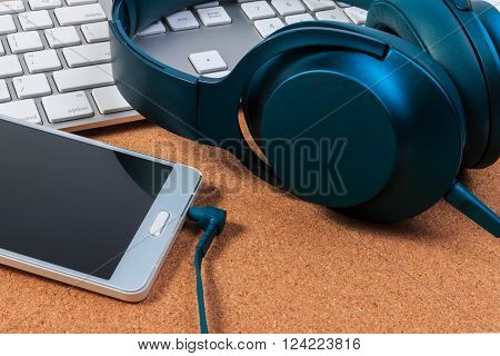 Headphones mobile phone and keyboard on craft board.