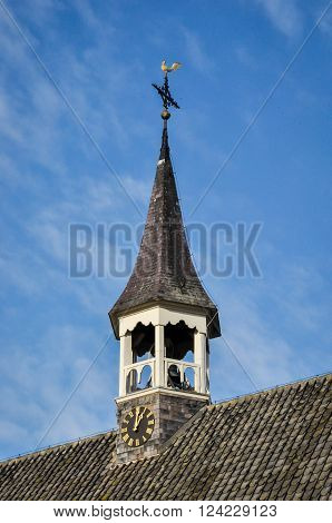 Closeup of a pointed church tower with clock belfry a cross and a golden weathervane dating from 1725 against the blue sky.