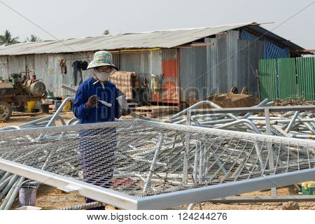 Petchaburi, Thailand - February 20, 2016: One woman worker paints wire metal fence in silver color at prepared area of outdoor construction on February 20, 2016 in Petchaburi, Thailand