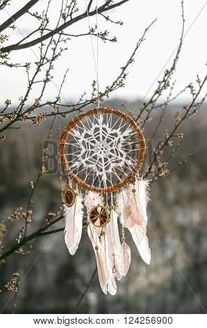 Handmade pink native american dream catcher on background of rocks and lake. Tribal elements feathers lace crochet snowflake doily