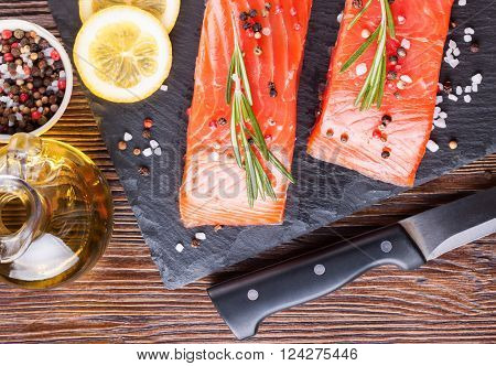 Raw salmon fillet and ingredients for cooking on a slade board and knife on  brown wooden background.