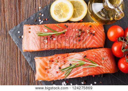 Raw salmon fillet and ingredients for cooking on a slade board and  brown wooden background. Top view