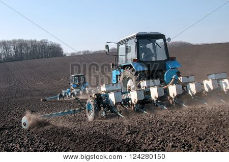 Blue tractor with sower on the field in bright sunny spring morning