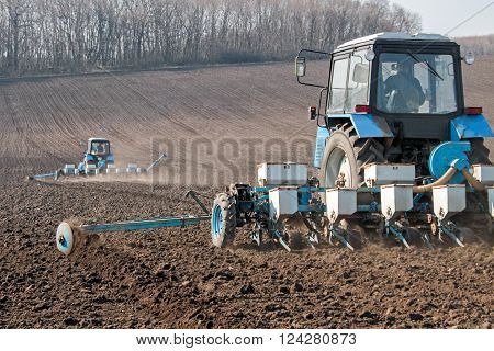 Blue tractor with sower on the field in bright sunny spring morning