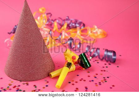 Birthday hat with serpentine streamer and noise makers on pink background