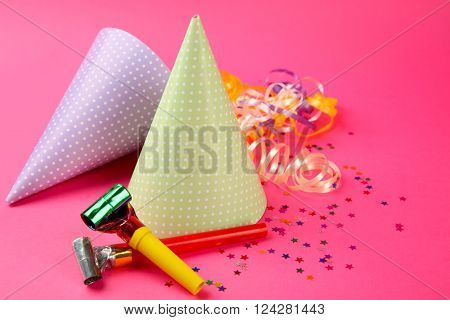Two dotted Birthday hats with serpentine streamer and noise makers on pink background