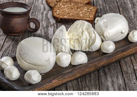 mozzarella balls on a dark board and clay cup with milk on an old rustic table top view