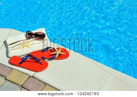 Flip-flops sunglasses towel starfish on the swimming pool.