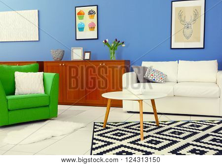 Modern living room interior with white sofa, coffee table, big graphic carpet, green chair and canvases on the blue wall