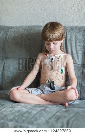Child sitting on the sofa. Heart cardiogram or monitoring of cardiac performance using Holter.