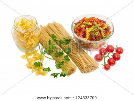 Uncooked dried long pasta two varieties colored spiral pasta and farfalle pasta sprigs of parsley and cluster of cherry tomatoes on a light background