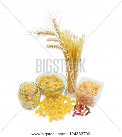 Uncooked dried long pasta and wheat spikes in glass other pasta different varieties shapes and colors on a light background