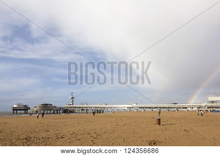 Scheveningen, Netherlands, 27 march 2016: people on beach near scheveningen pier with cloudy sky and rainbow in afternoon sun