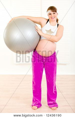 Sorridente bella donna incinta in casa tenendo palla fitness nelle mani