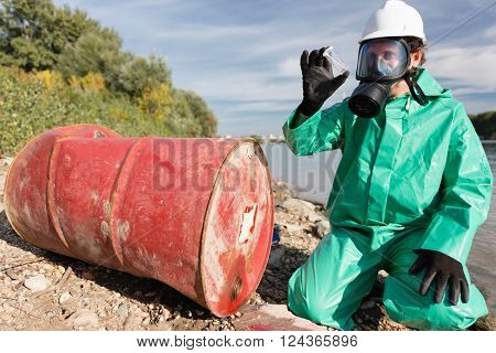 Pollution control official looking at sample of leaked chemicals collected by the river