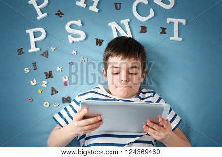 seven years old child lying with tablet and letters on blue background