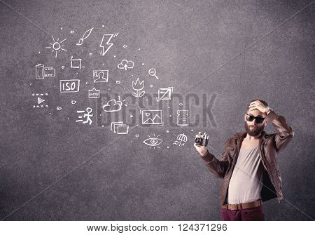 An elegant hipster guy trying to use a vintage camera with camera settings icons drawn on wall, like flash, white balace or ISO value concept