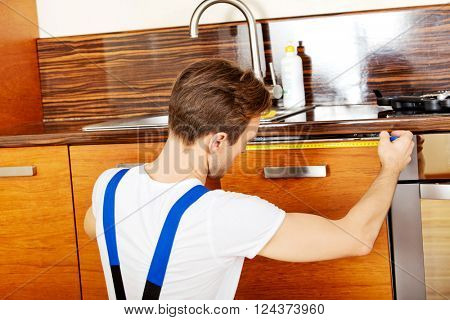 Young repair man measuring kitchen cabinet