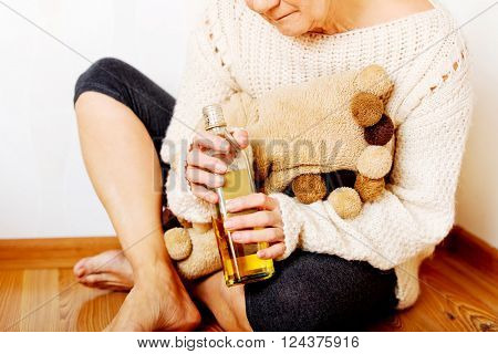 Elderly sad woman sitting in the corner and drinking whiskey