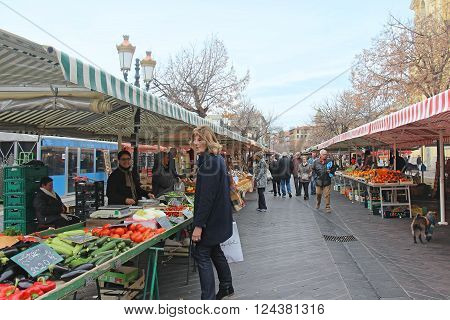 NICE FRANCE - FEBRUARY 03; Large French green market Cours Saleya with people walking around and buying food in Nice France - February 03 2016: Open air market overflown with fresh cheese herbs fruit and vegetables.