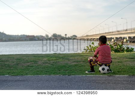 Songkhla Province, Thailand,  April 20, 2014 : A boy is sitting on his football in the park on Songkhla Lake. To wait for friends to play football together.