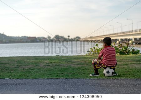 Songkhla Province, Thailand,  April 20, 2014 : A boy is sitting on his football in the park on Songkhla Lake. To wait for friends to play football together.