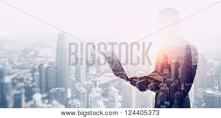 Double exposure photo bearded businessman wearing black shirt and glasses.Banker using contemporary notebook hands, work online banking.Panoramic view modern skyscraper city background