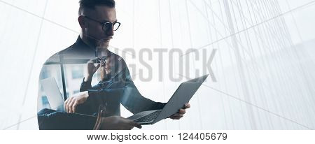 Double exposure bearded businessman wearing black shirt and glasses, holding contemporary notebook hands. Portrait young banker using laptop in modern office, skyscraper background.