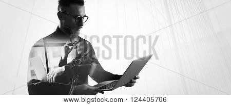 Double exposure bearded businessman wearing shirt and glasses, holding contemporary notebook hands. Portrait young banker using laptop in modern office, skyscraper background.