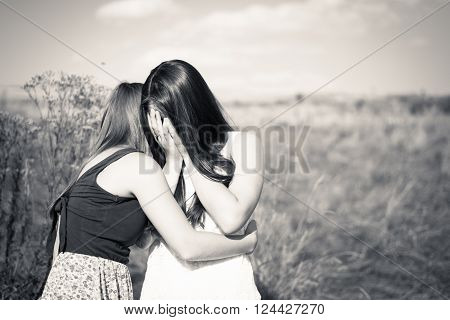 Black and white picture of one girl comforting and expressing feelings of compassion for another: beautiful young women girlfriends having difficult times on summer outdoors background