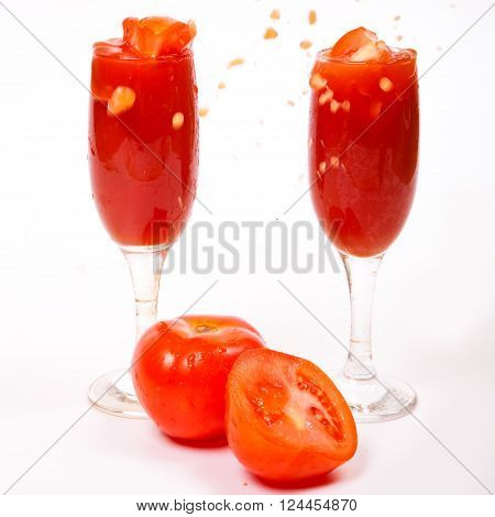 Splashes of fresh tomato juice in a glass and cut in half the tomatoes on a white background