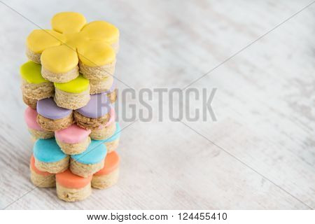 Colorful flower form homemade fondant covered cookies on a white wooden background