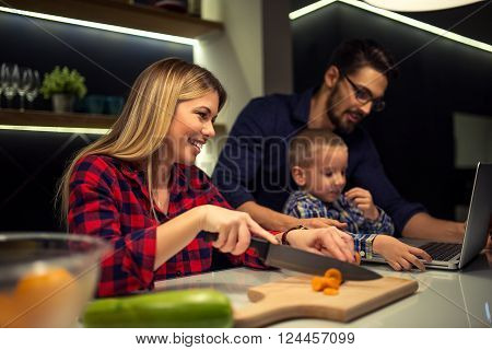 Mother preparing food while dad and son using laptop. Selective focus.