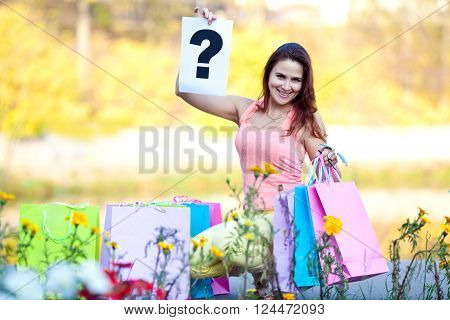Cheerful beautiful girl with shopping bags holding a question mark in the autumn park