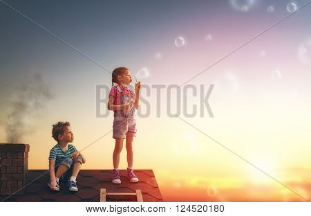 happy childhood! boy and girl playing on the roof. child blowing soap bubbles.