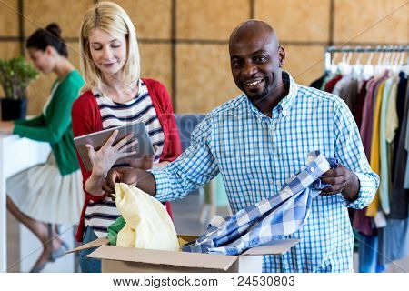 Colleagues using digital tablet while sorting clothes from donation box in the office