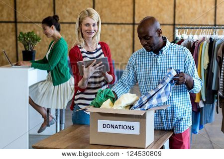 Colleagues using digital tablet while sorting clothes from donation box in the office