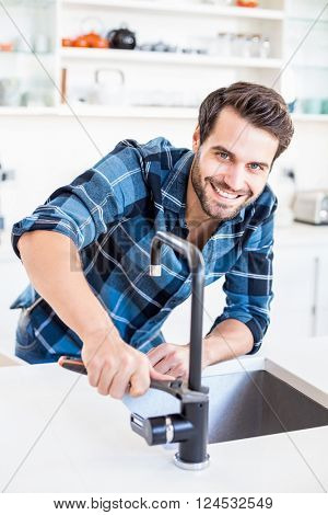 Portrait of happy man fixing tap with tool in the kitchen at home